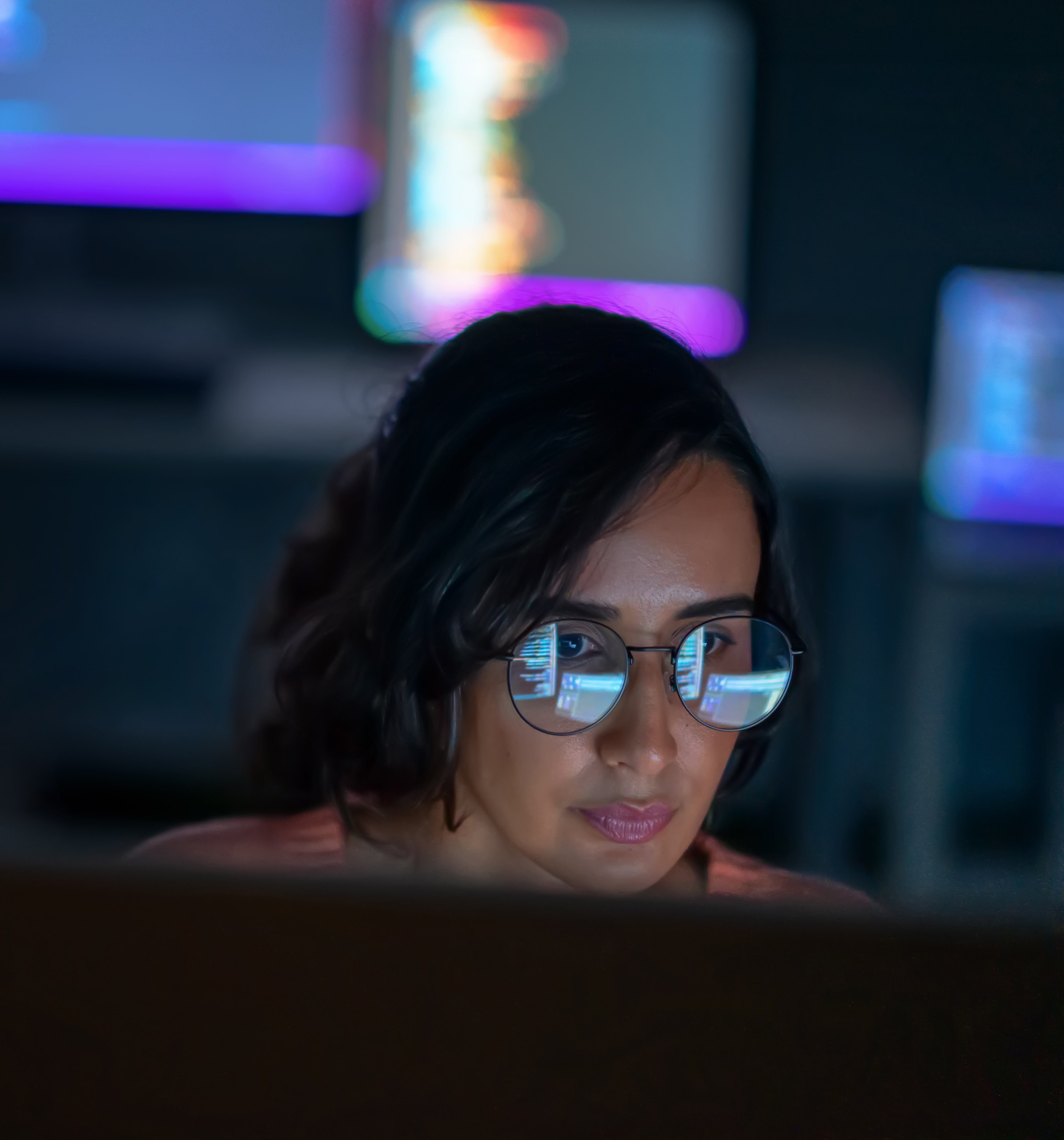 Une femme regarde des écrans d’ordinateur dans une pièce sombre.