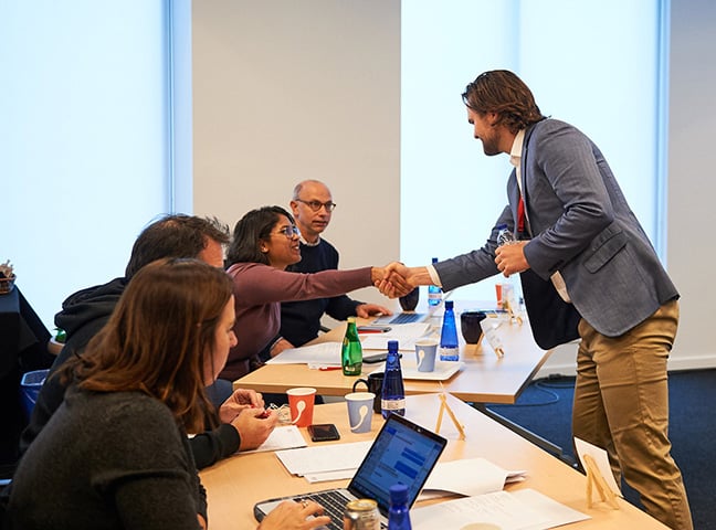 3. Two people shake hands while the team looks on.