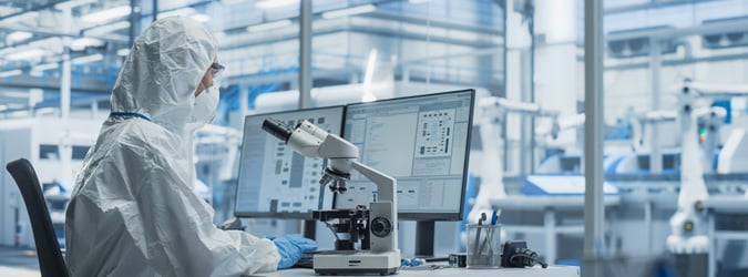 R&D scientist in clean sterile coveralls using a microscope.