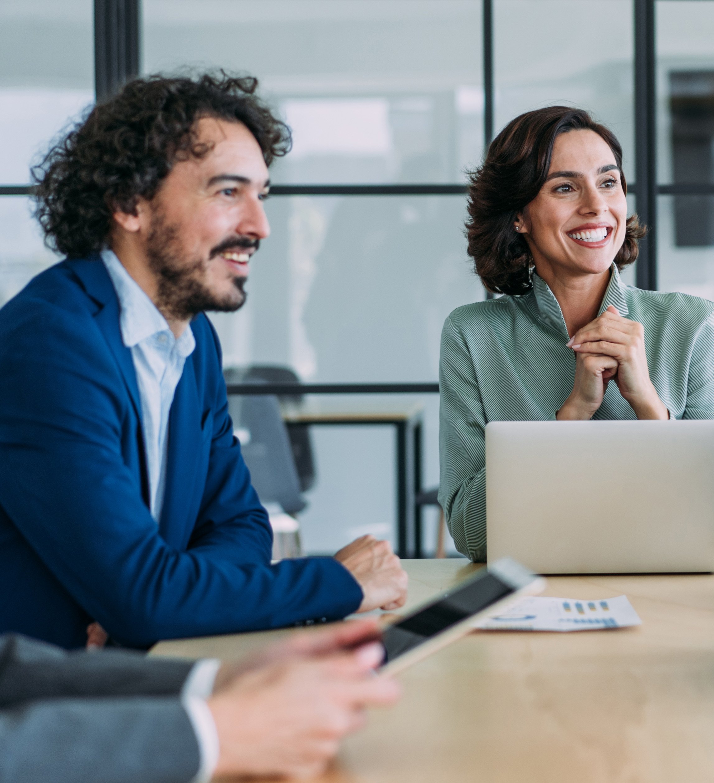 Two professionals, a man and woman, discuss information on a curved computer monitor in a tech-forward office setting.