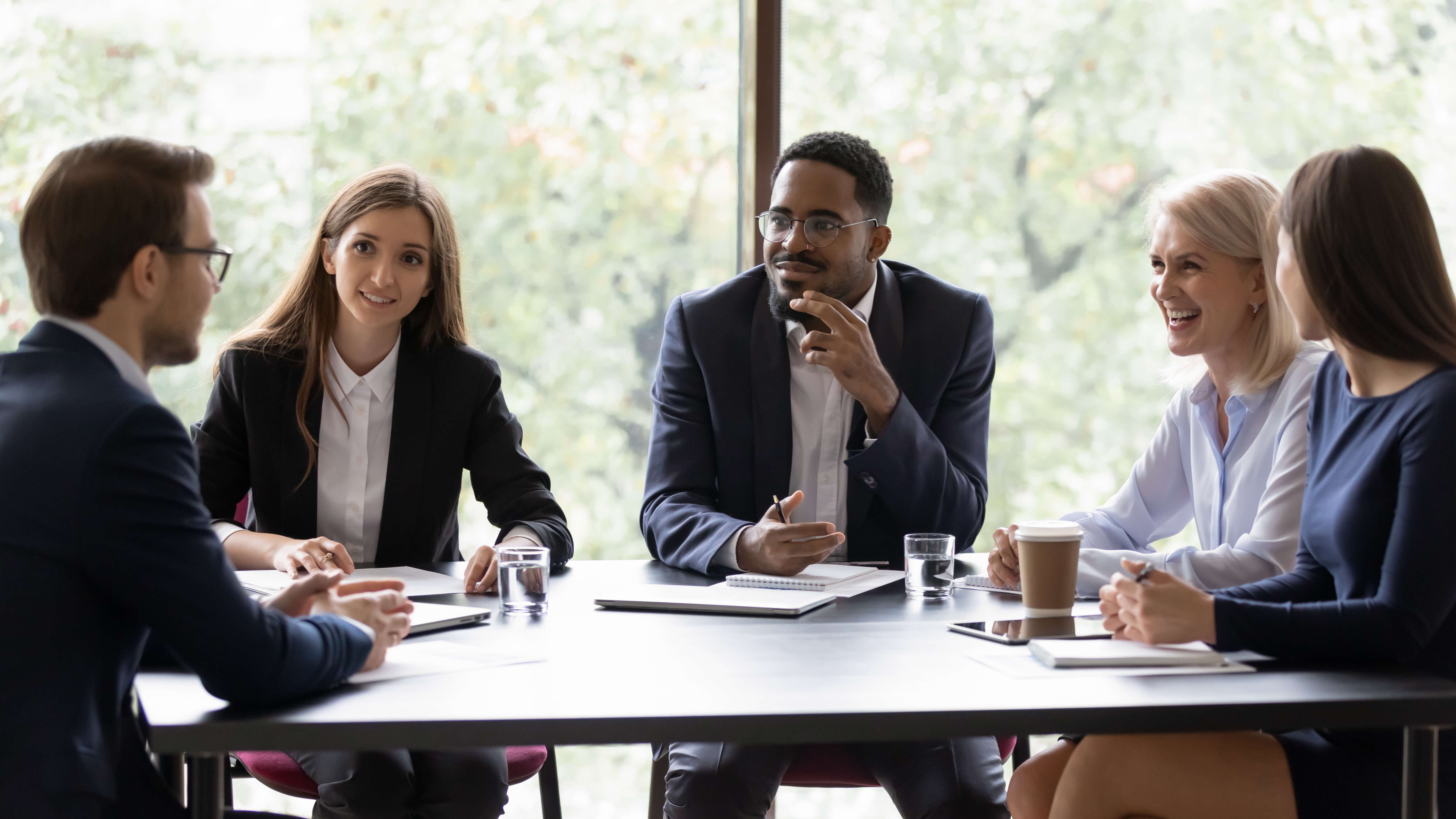 A group of diverse business professionals sitting around a table and having a discussion in a meeting room.