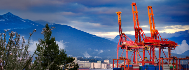 A view of the Port of Vancouver, a large shipping port, with mountains in the background.