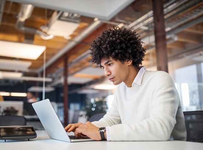 A young businessman working on a laptop in an office setting.