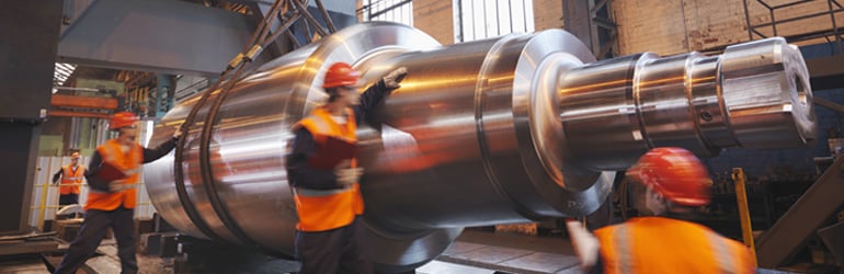 Engineers wearing personal protective equipment in a factory standing against a large, finished steel product.