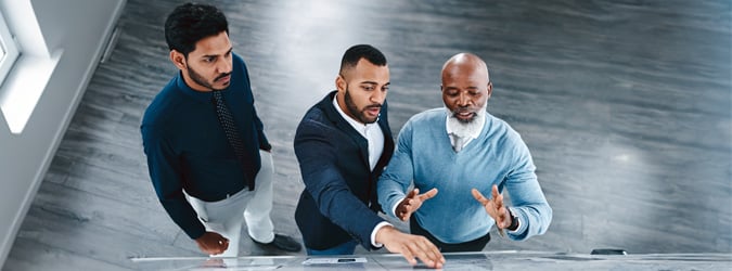 High angle shot of three businessmen brainstorming together on a whiteboard in an office.