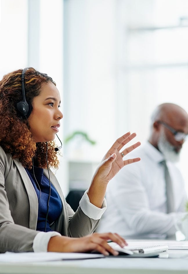 Dans un espace de travail, des employées d’un centre d’appels portant un casque d’écoute travaillent à un bureau sur lequel est posé un écran d’ordinateur.
