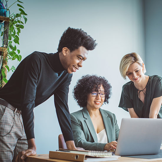 Three people are viewing information on a laptop as they collaborate.