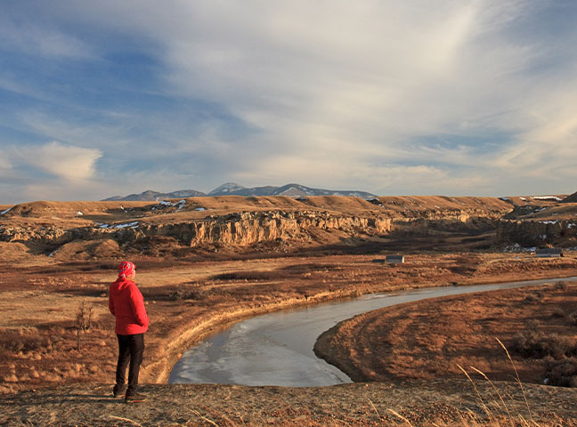 Un homme admire la vue sur les collines rocheuses et une rivière au parc provincial Writing-On-Stone en Alberta, au Canada.