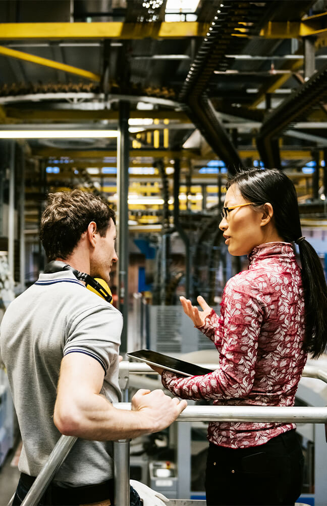 Deux ingénieurs, homme et femme, discutent dans une usine.