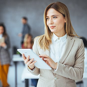 A standing female professional in a grey suit, holding a tablet.