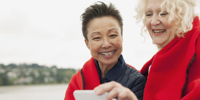 Deux amies, le sourire aux lèvres, qui regardent leur téléphone tout en marchant