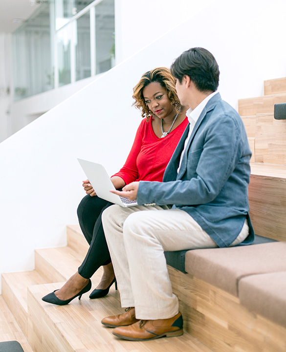 Two colleagues sitting and looking at computer on stairs