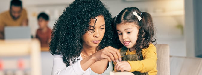 Une mère et sa fille mettent des pièces de monnaie dans une tirelire à la table de leur cuisine.