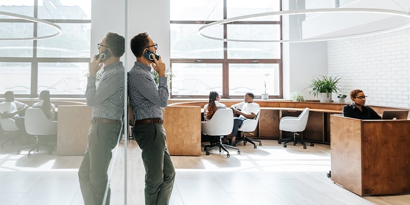 Un homme d’affaires appuyé contre un mur dans un décor de bureau parle au téléphone cellulaire.