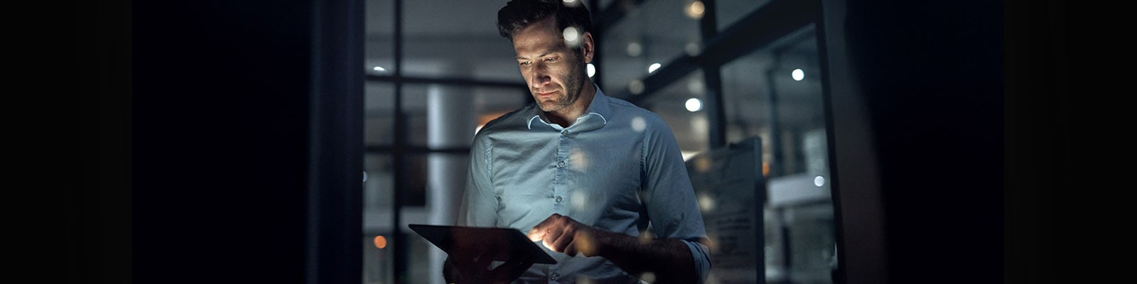 Un homme d’affaires utilise une tablette alors qu’il est debout dans un bureau sombre.