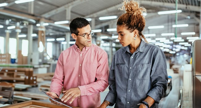 Female and male professionals talking at a manufacturing facility, depicting modern manufacturing tech and machinery.