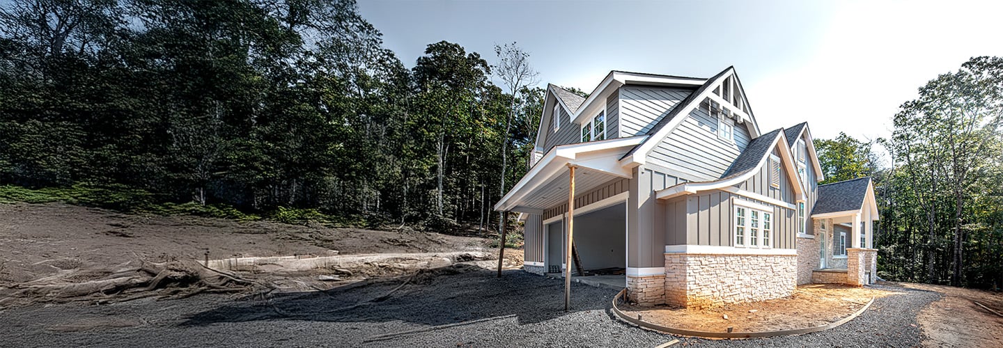 A grey two-story house with a garage and gravel driveway.