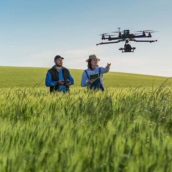 Two people dressed in farming attire operating a drone in a field.