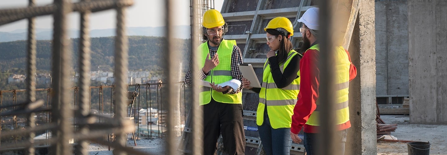 Three workers in yellow vests at a construction site.