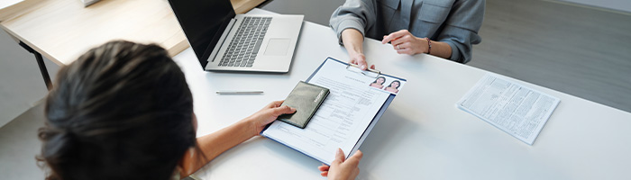 Person handing over a passport and application form to another person sitting across a table.