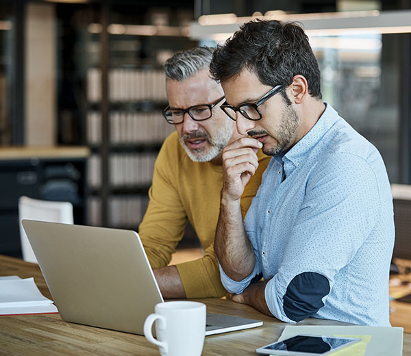 Two male business professionals focusing on a laptop screen in a modern office setting.