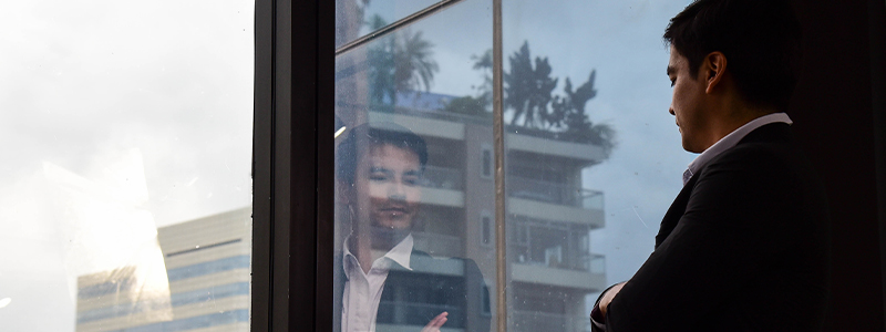 Un homme d’affaires regarde un autre édifice à travers une fenêtre. Son image se reflète dans la fenêtre.