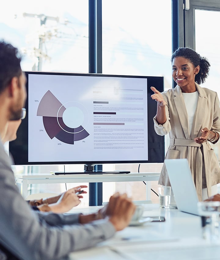 Businesswoman presenting to colleagues with a graph on the tv screen in a modern boardroom.