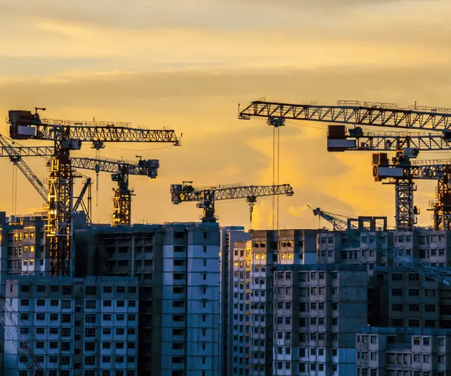 Bâtiments en construction avec des grues en arrière-plan au coucher du soleil.
