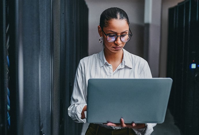 A young businesswoman holding a laptop working in a server room.