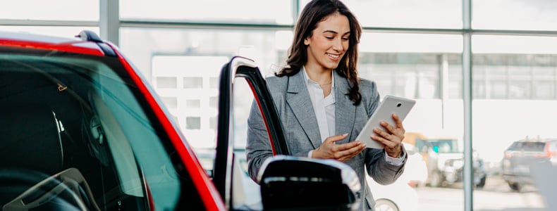 person looking at a tablet beside a brand new car in dealership