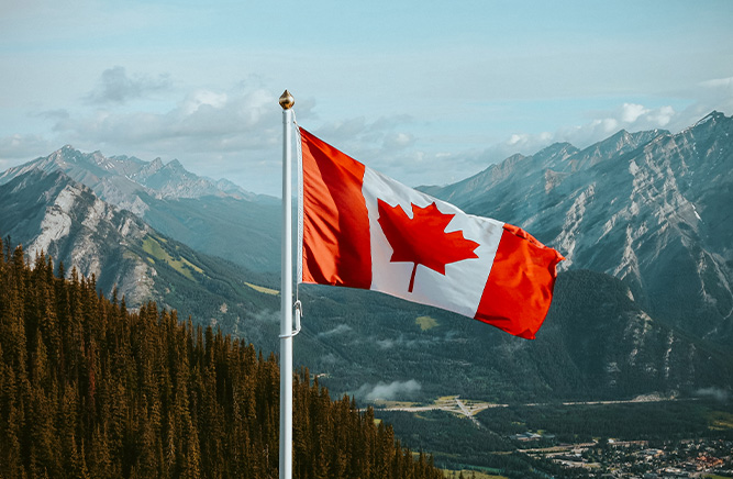 Canadian flag waving against a backdrop of mountains.
