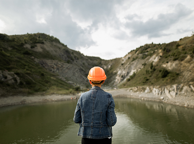 Un travailleur coiffé d’un casque de construction devant une fosse minière remplie d’eau.