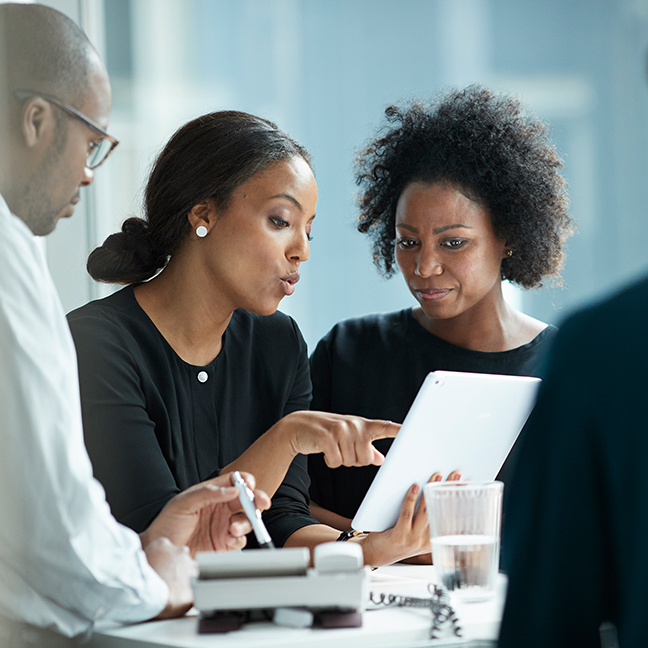 Four professionals discussing and standing around a desk in an office setting.